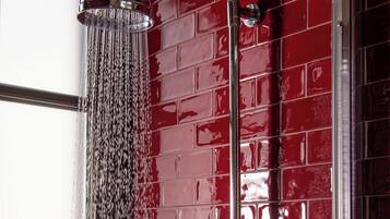 Eine Dusche mit Duschkopf aus Chrom und mehreren Düsen vor einer roten Fliesenwand.