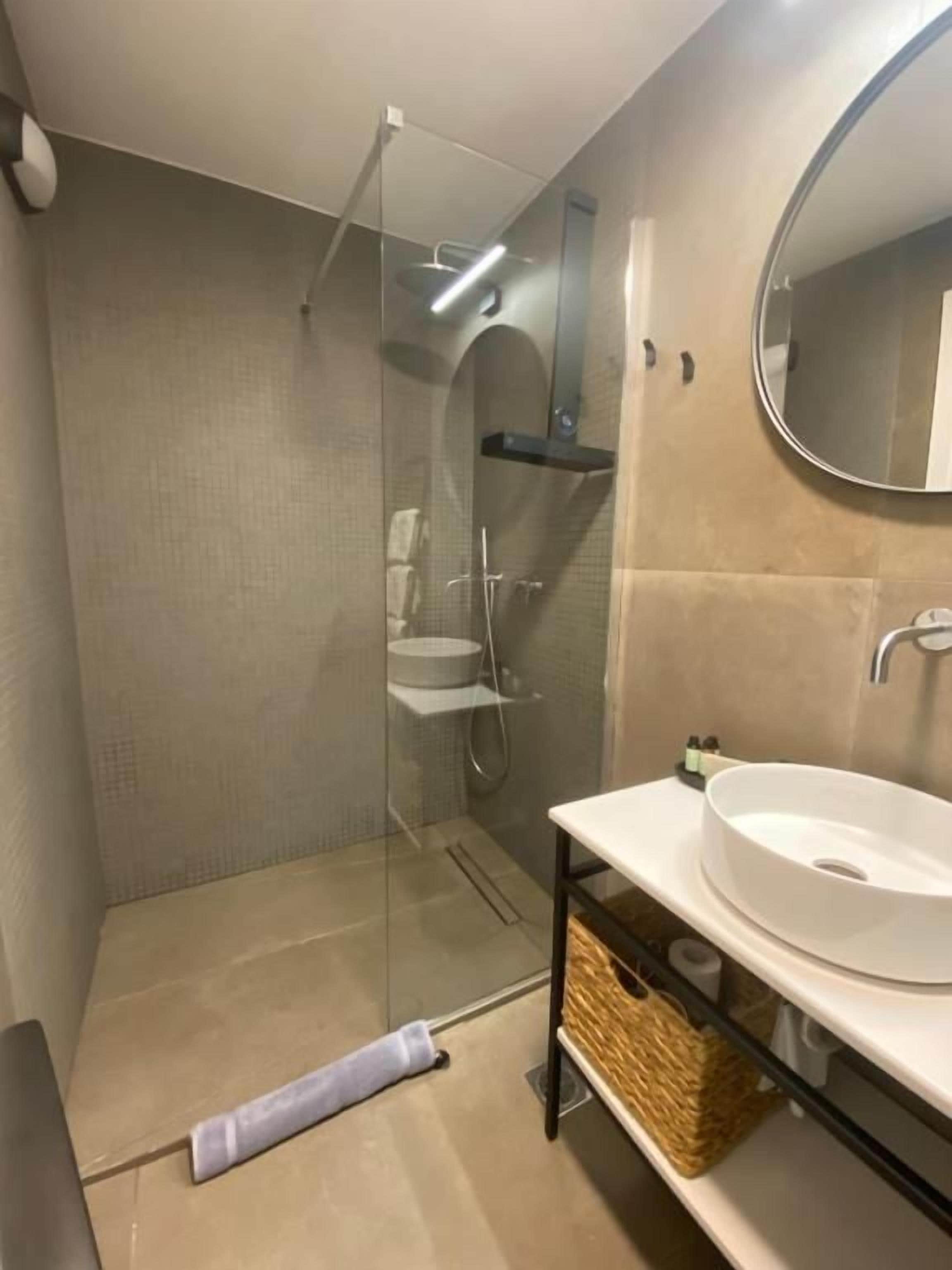 Un baño con ducha envuelta en cristal, un lavamanos blanco y un espejo.