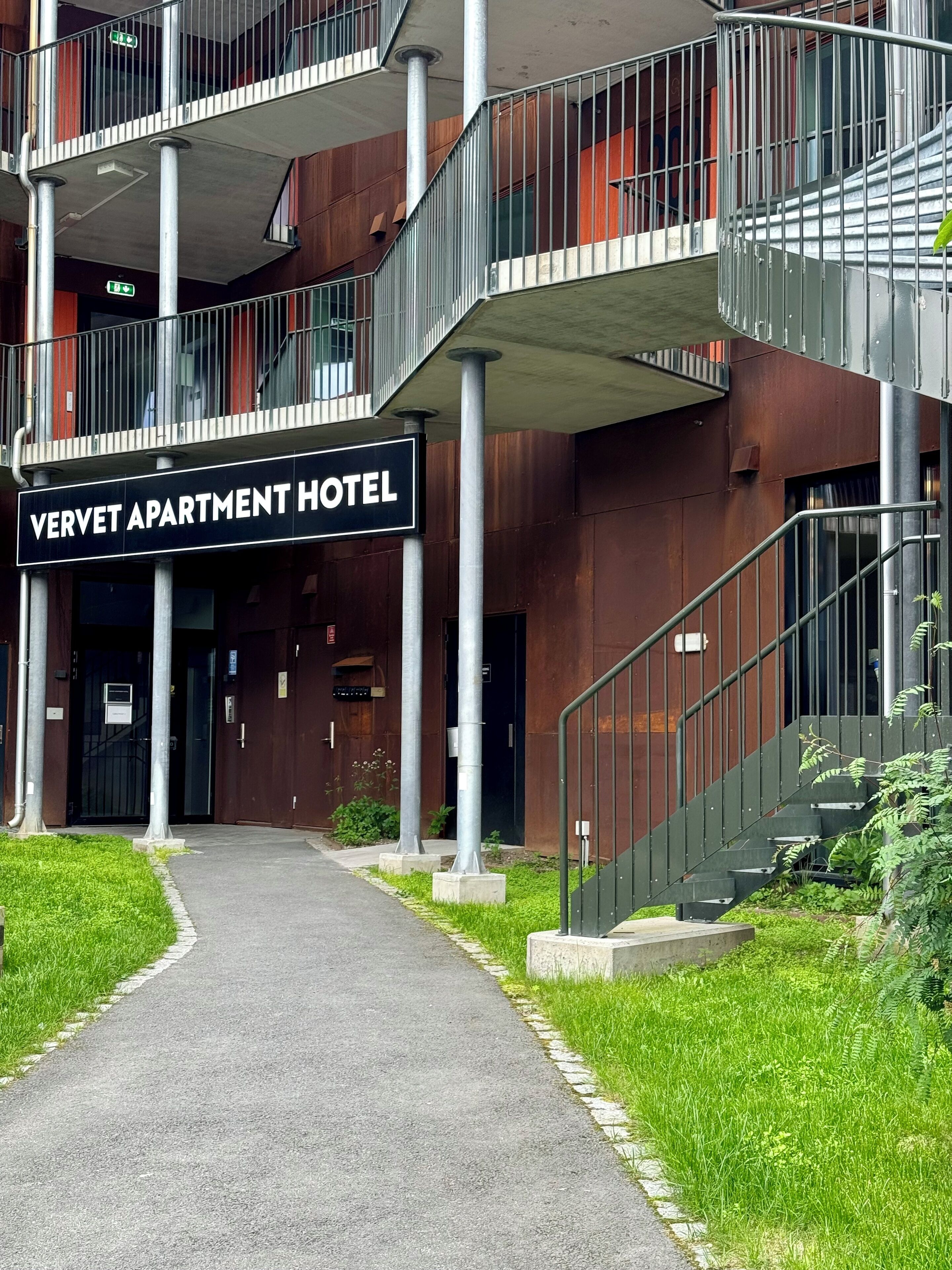 Moderni rakennus, jonka yläpuolella on kyltti, jossa lukee ”Vernet Apartment Hotel”. Siinä on keskeisellä paikalla sijaitseva portaikko, useita parvekkeita ja hyvin hoidettu sisäänkäyntialue.