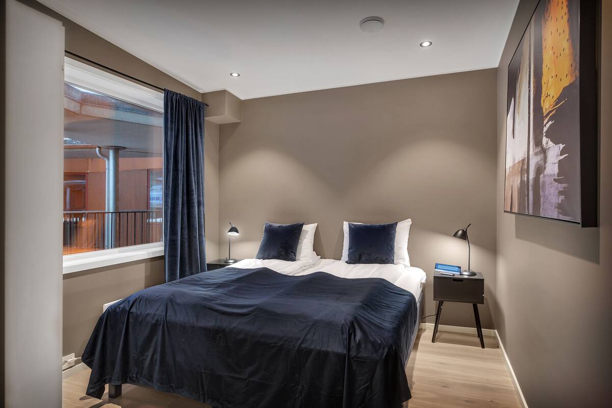 A bedroom with a large bed, a nightstand, a window with curtains, and a painting on the wall.