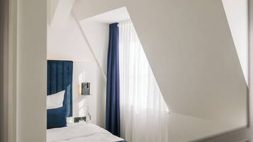 Una habitación de hotel moderna con cama, mesita de noche, lámpara y ventana con cortinas.