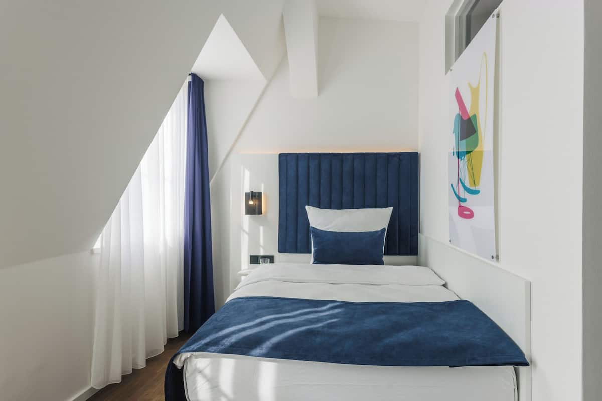 A modern hotel room with a bed, a nightstand, and a window with curtains.