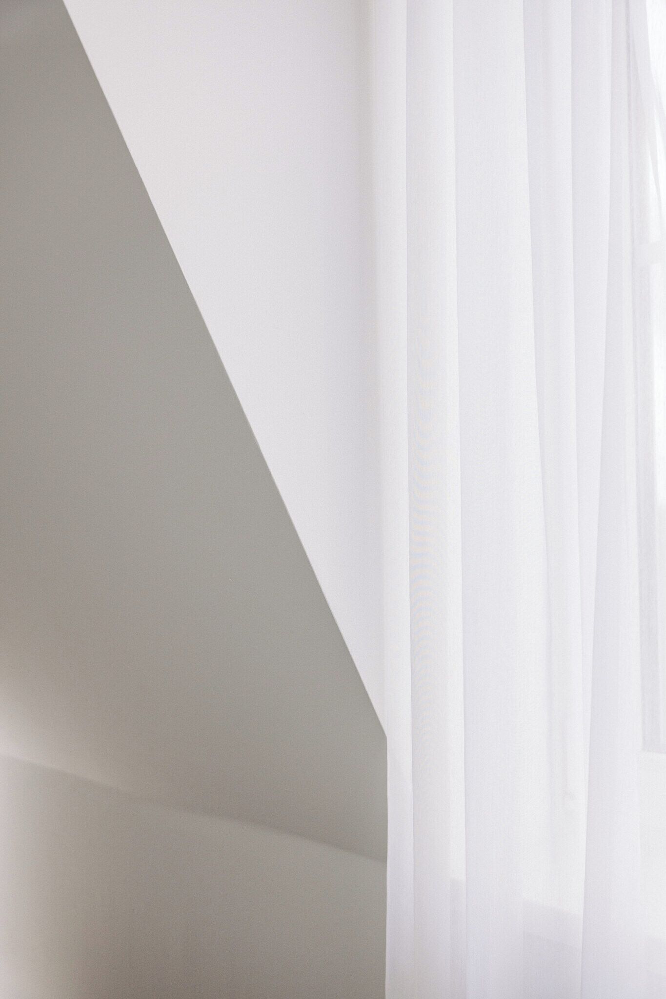 Una habitación con techo inclinado y cortinas blancas y translúcidas.