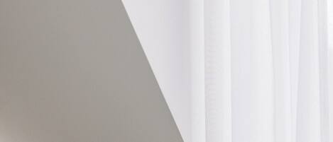 Una habitación con techo inclinado y cortinas blancas y translúcidas.