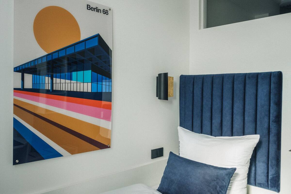 A modern bedroom with a bed, a blue headboard, a wall-mounted artwork, and a window.