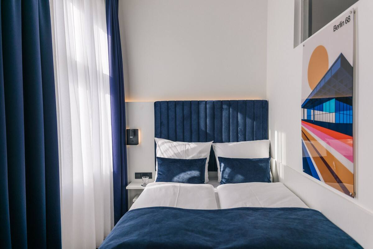 A hotel room with a bed, a nightstand, a lamp, and a painting on the wall.