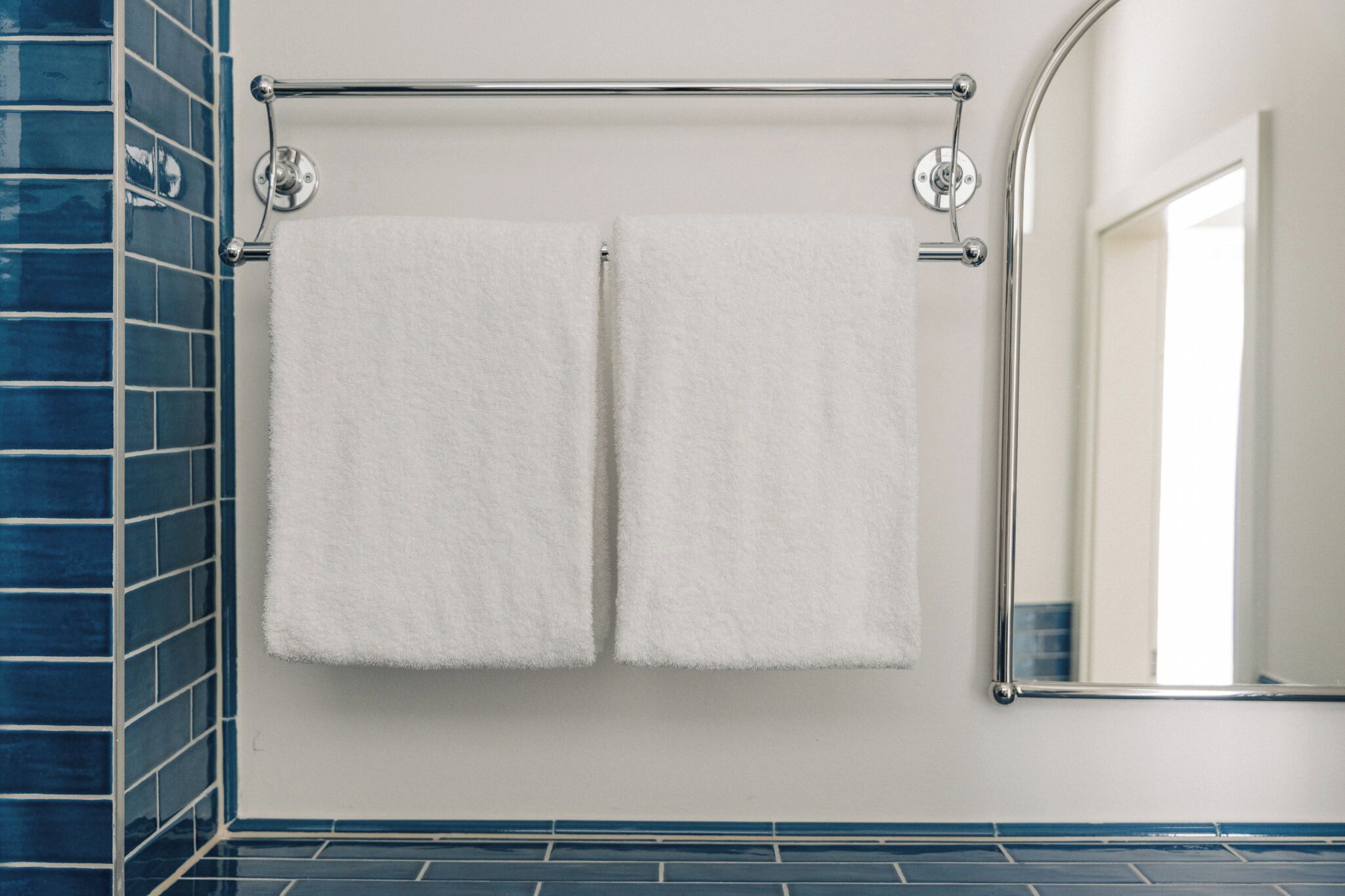 A bathroom with a towel rack holding two white towels, a blue-tiled wall, and a mirror.