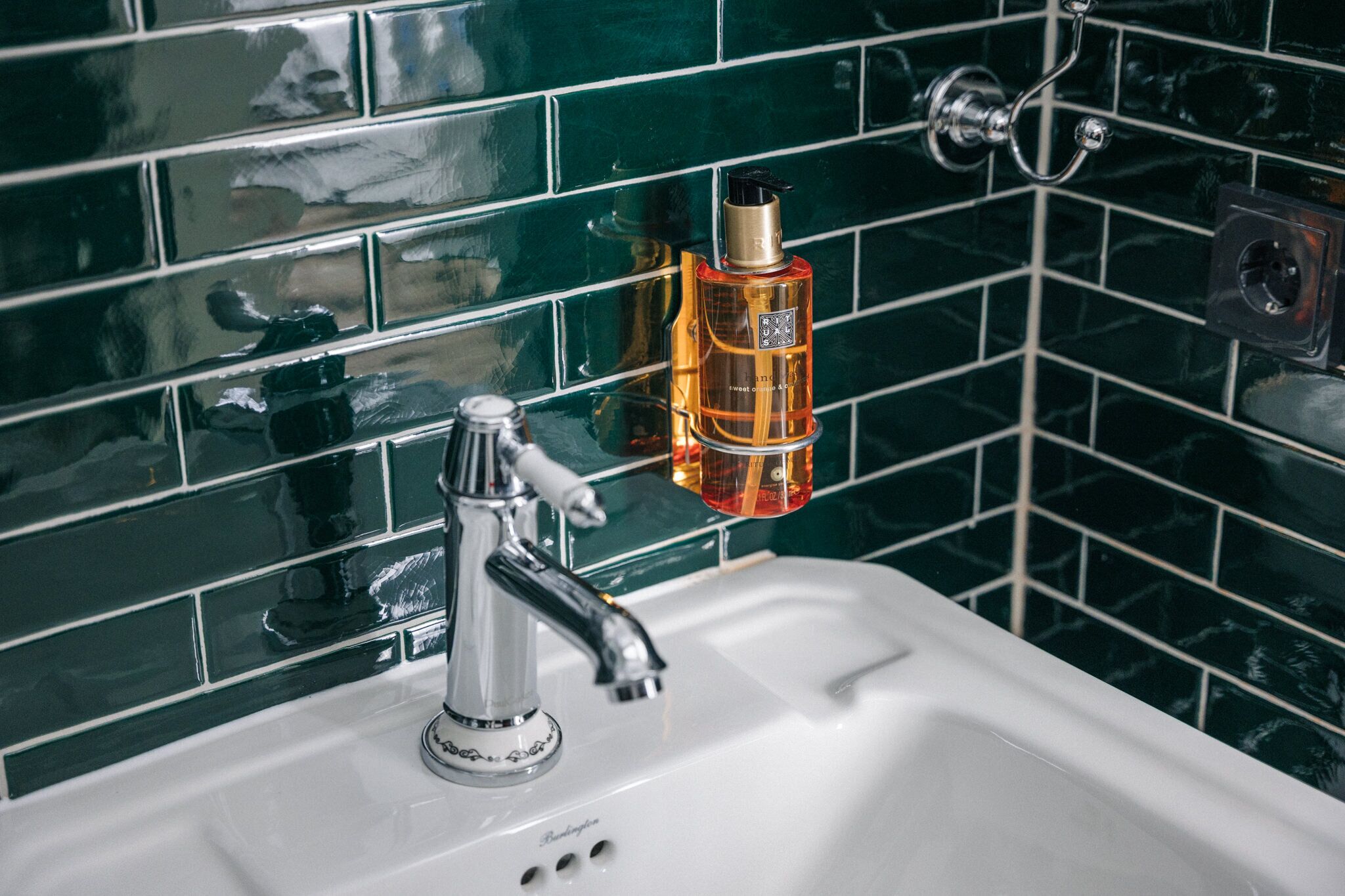 A bathroom with a white sink, a chrome faucet, and a bottle of hand soap on the wall.