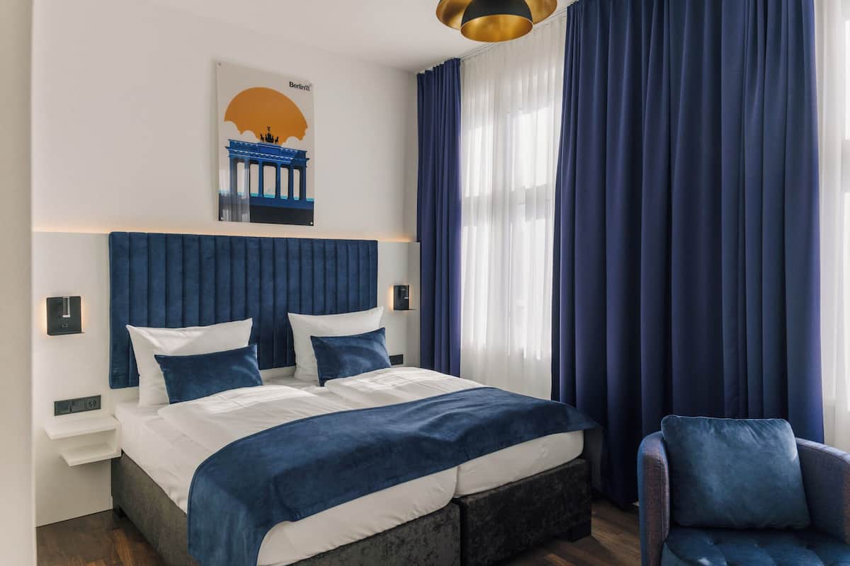 A modern bedroom with a large bed, blue curtains, and a cityscape artwork on the wall.