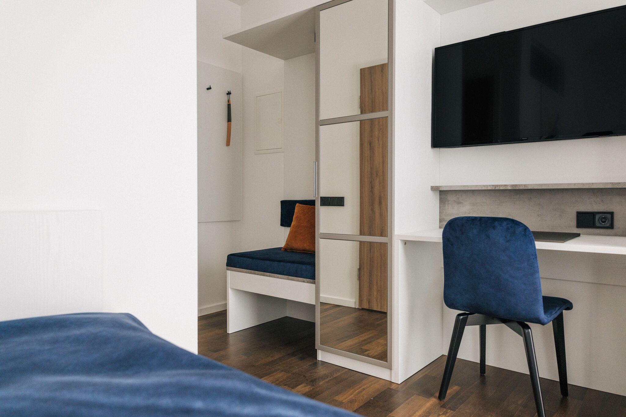 Una habitación moderna con una cama, un escritorio con silla, un televisor y un armario.