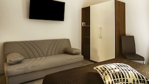 A modern hotel room with a sofa, a bed, a wardrobe, and a TV. - Residenza Tupini S.Pietro Suites (Rome)