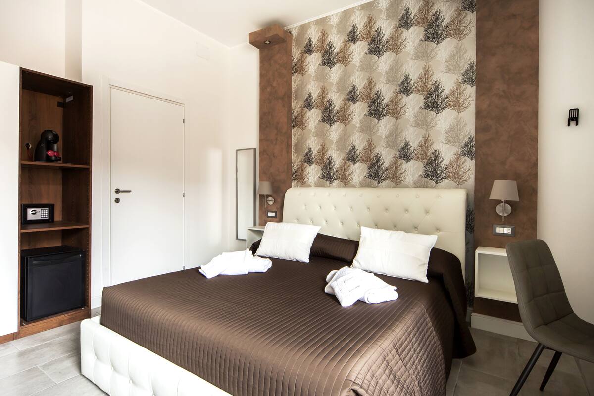 A neatly arranged hotel room with a large bed, a wardrobe, a desk, and a chair.