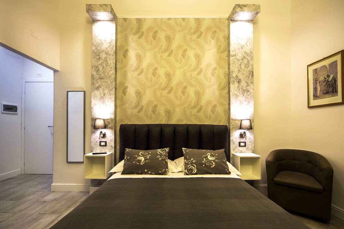 A hotel room with a large bed, two bedside lamps, a chair, and a framed picture on the wall.