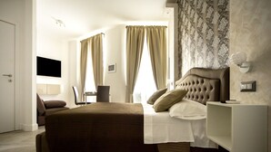 A modern bedroom with a large bed, a bedside table, a chair, and a TV mounted on the wall. - Residenza Tupini S.Pietro Suites (Rome)