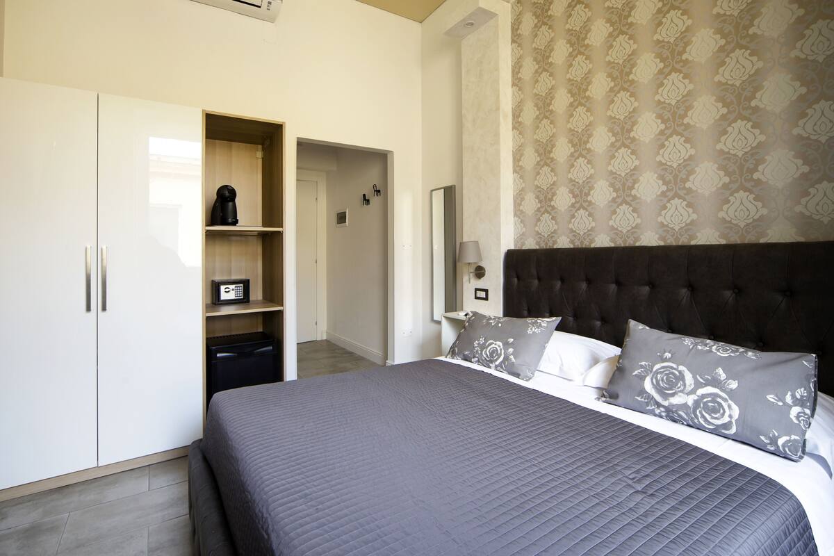 A bedroom with a large bed, a wardrobe, a built-in shelf with a coffee maker, and a patterned wall.