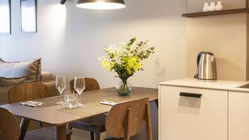 A modern dining area with a wooden table, chairs, a vase with flowers, and a kettle on a cabinet.