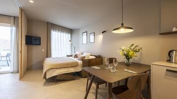 Una habitación de hotel moderna con una cama, una mesa de comedor con sillas, una pequeña cocina y un televisor montado en la pared.