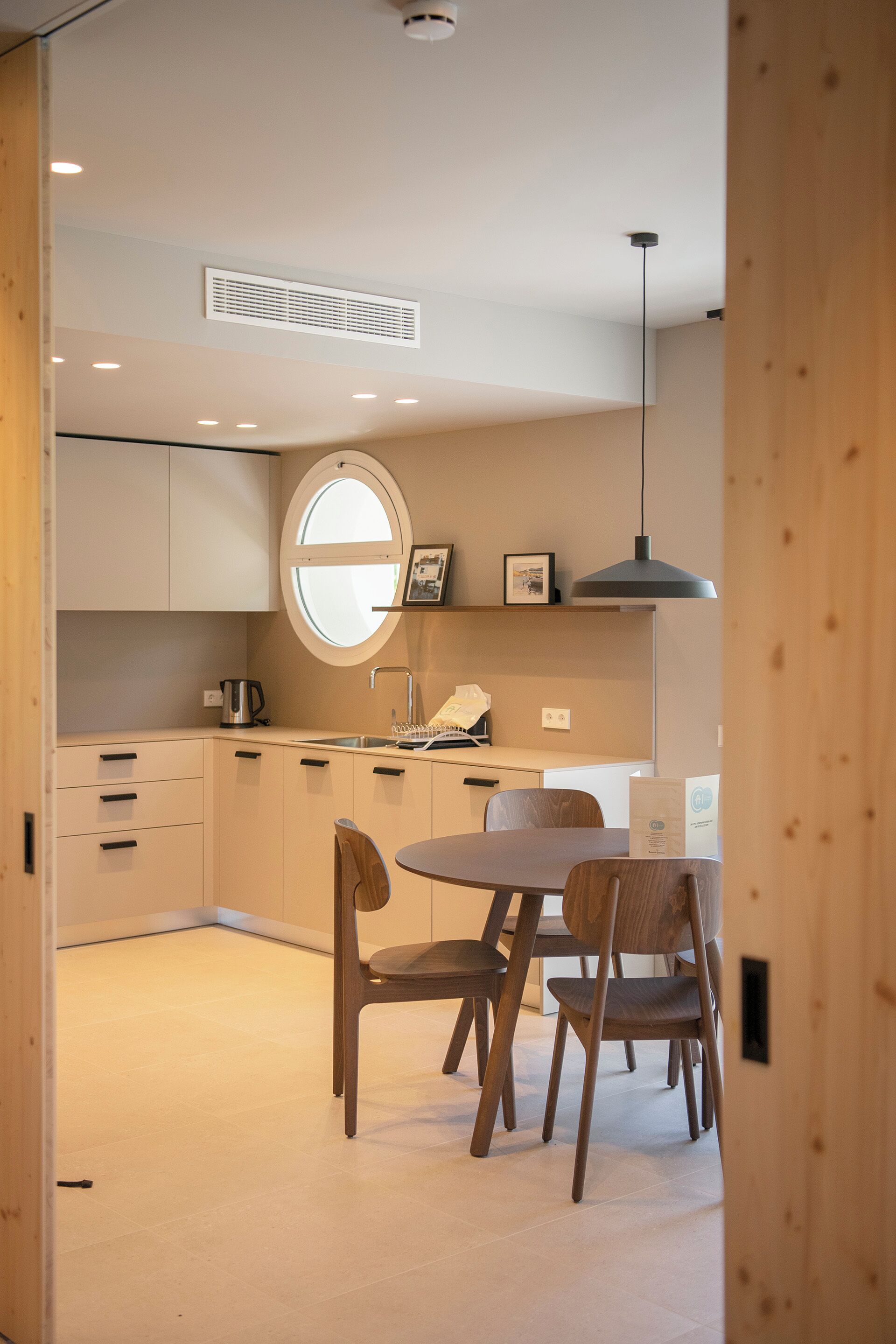 Una cucina moderna con una finestra rotonda, mobili in legno e un'area pranzo con due sedie e un tavolo.