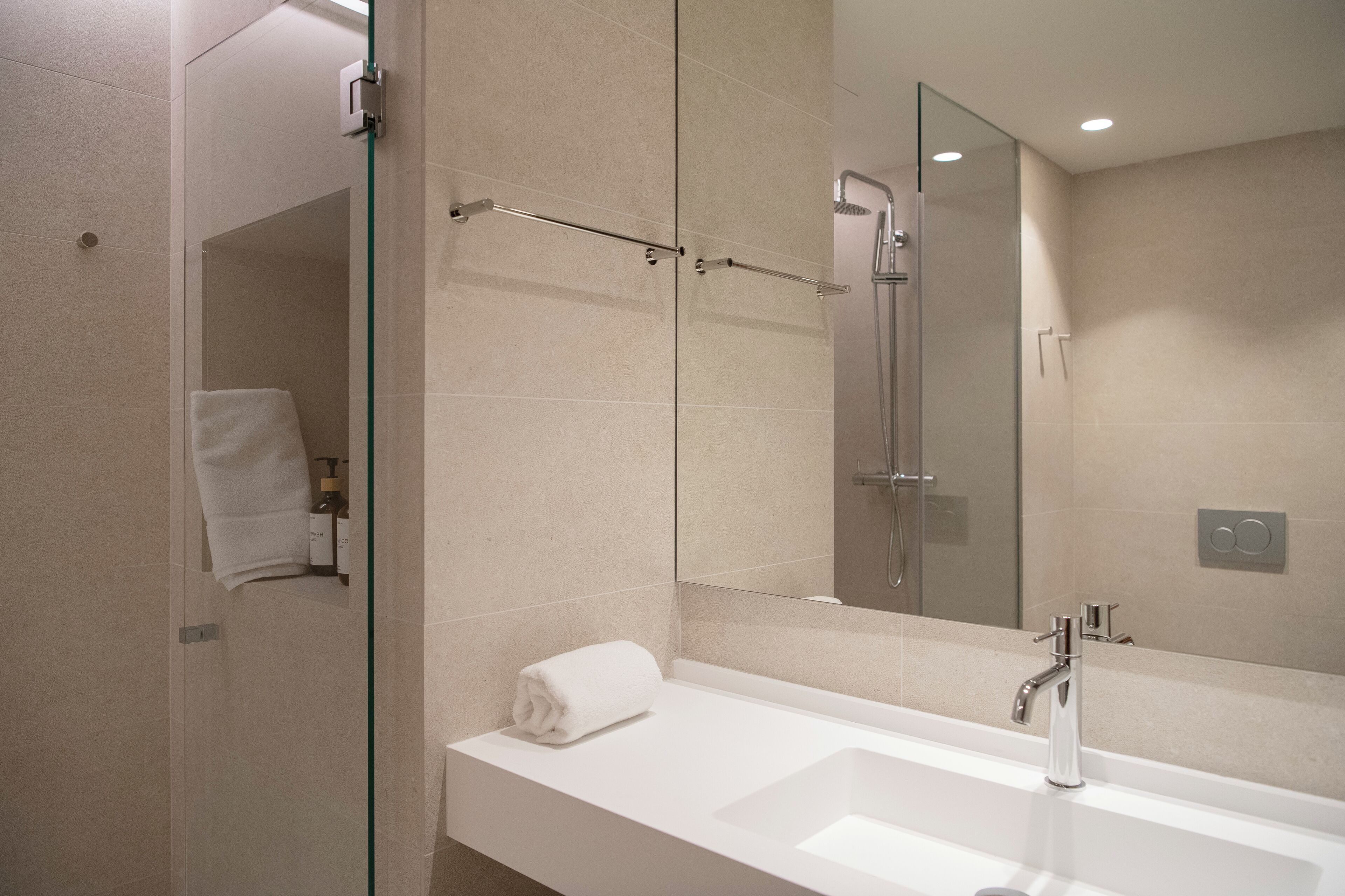 Un baño moderno con cabina de ducha de vidrio, un lavabo blanco y un espejo grande.