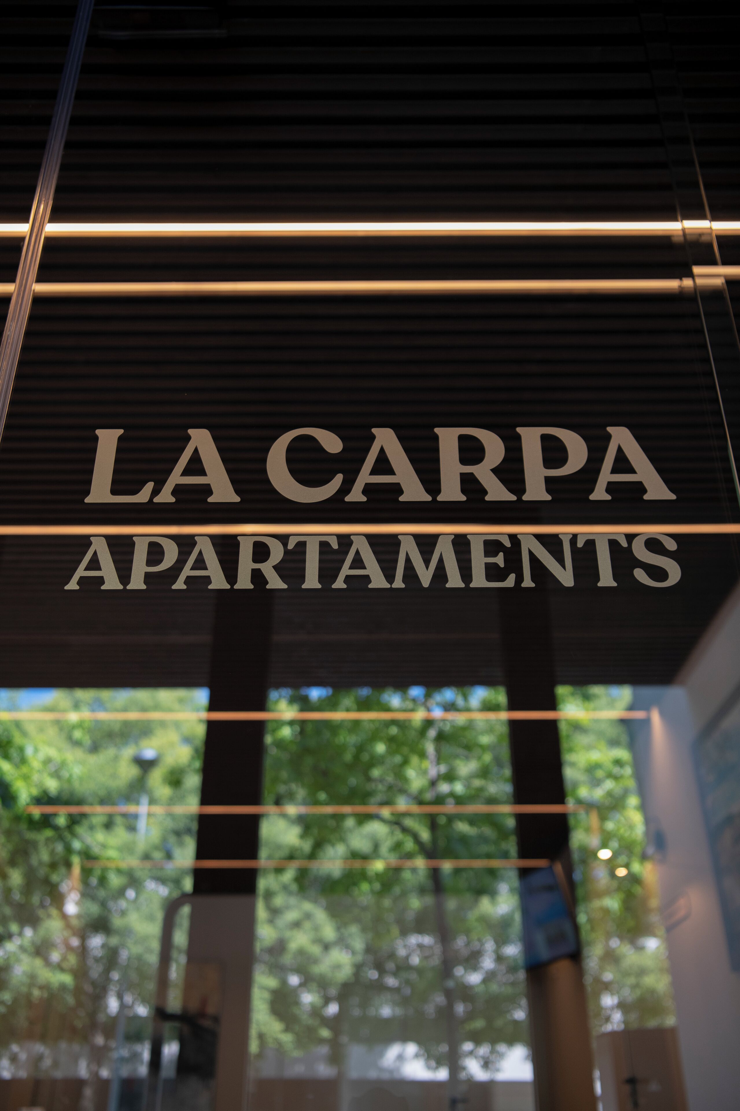 A sign for "LA CARPA APARTMENTS" with a view of trees through the window.