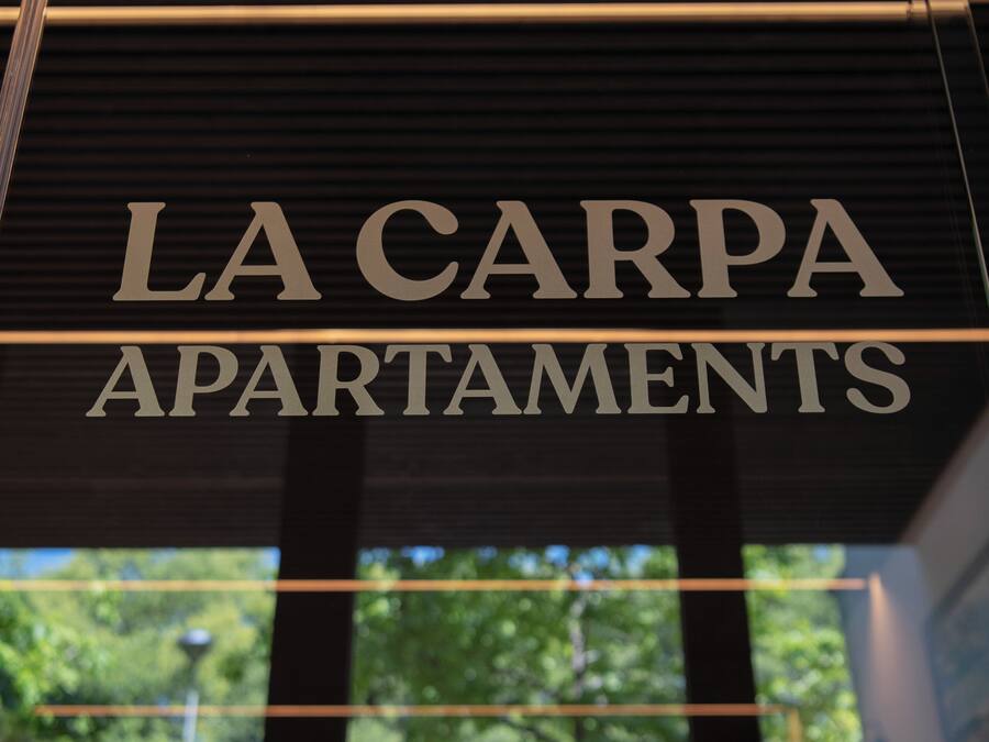 A sign for "LA CARPA APARTMENTS" with a view of trees through the window.