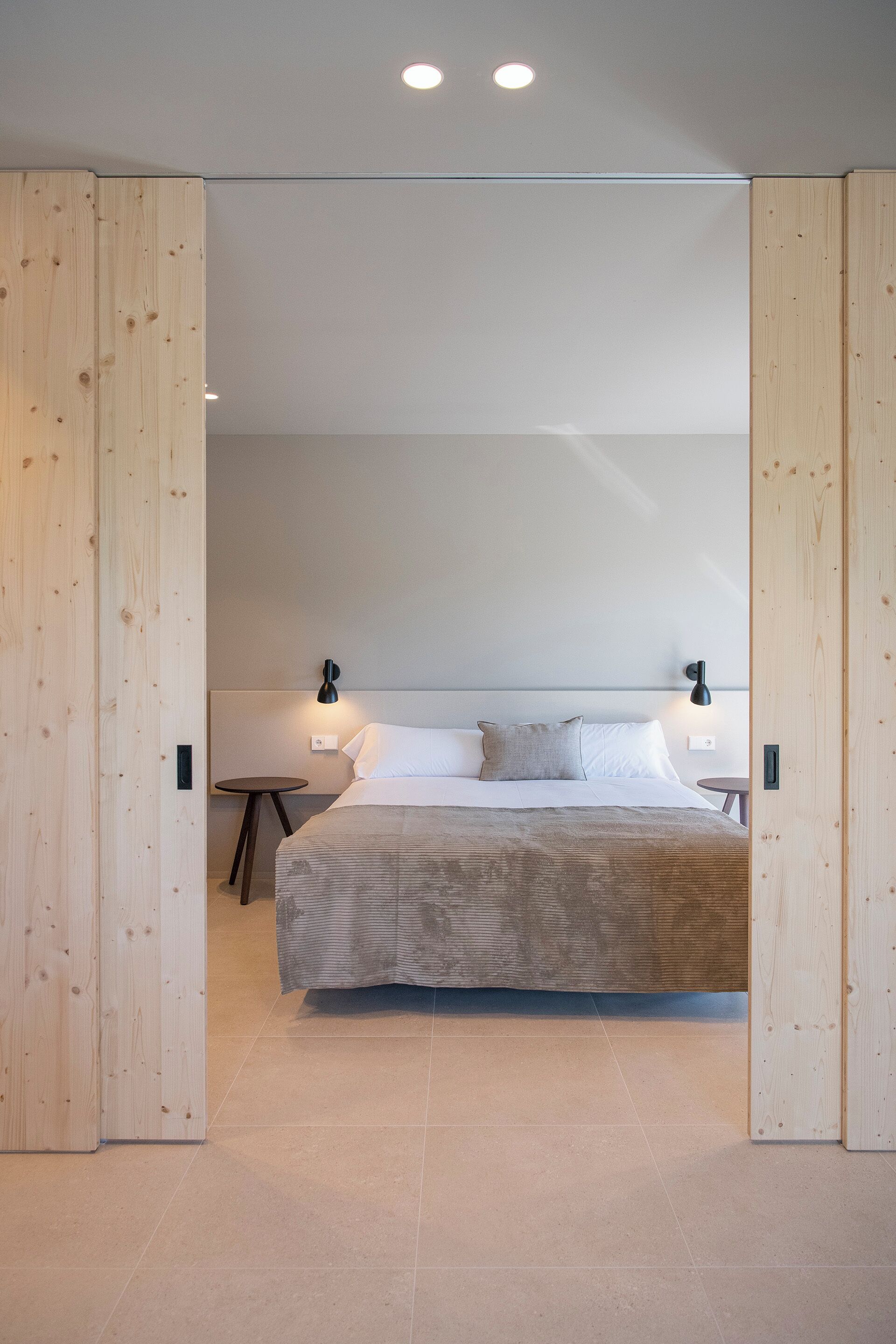 A modern bedroom with a large bed, wooden paneling, and two bedside lamps.