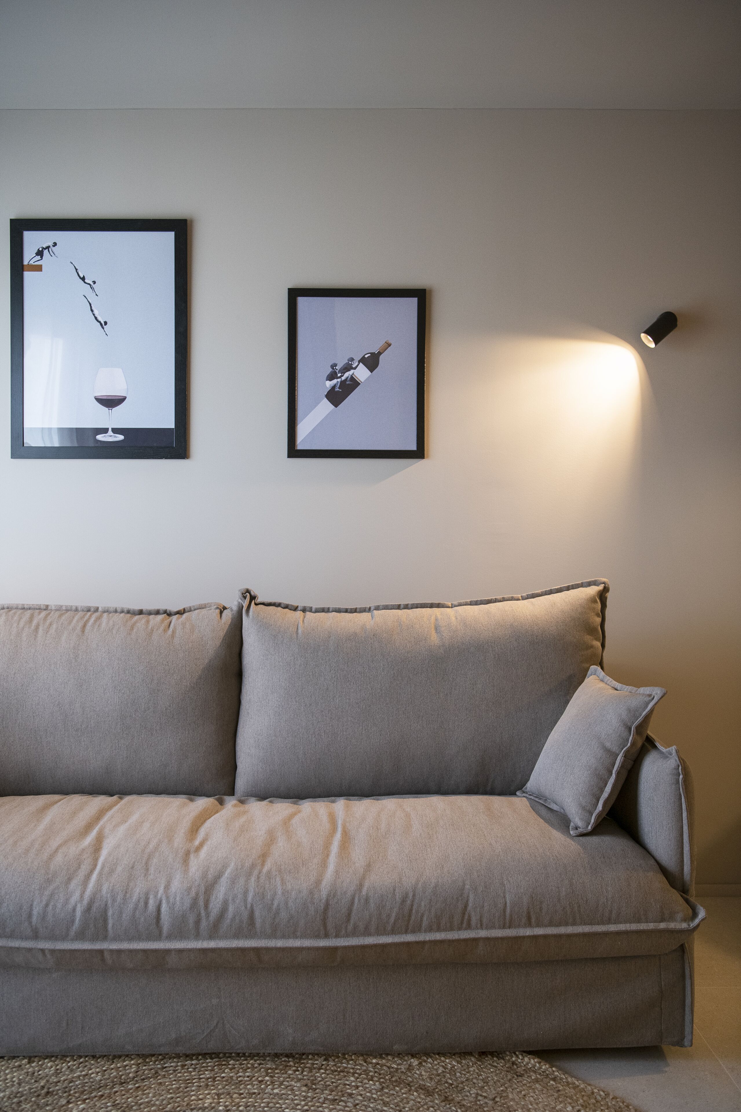 Een sofa in neutrale tinten met een gebreide plaid, twee kunstwerken in lijsten aan de muur, en een vloerlamp die sfeerverlichting geeft.