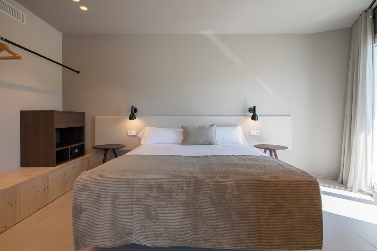 Une chambre moderne avec un grand lit, des tables de chevet, un banc en bois et une armoire.