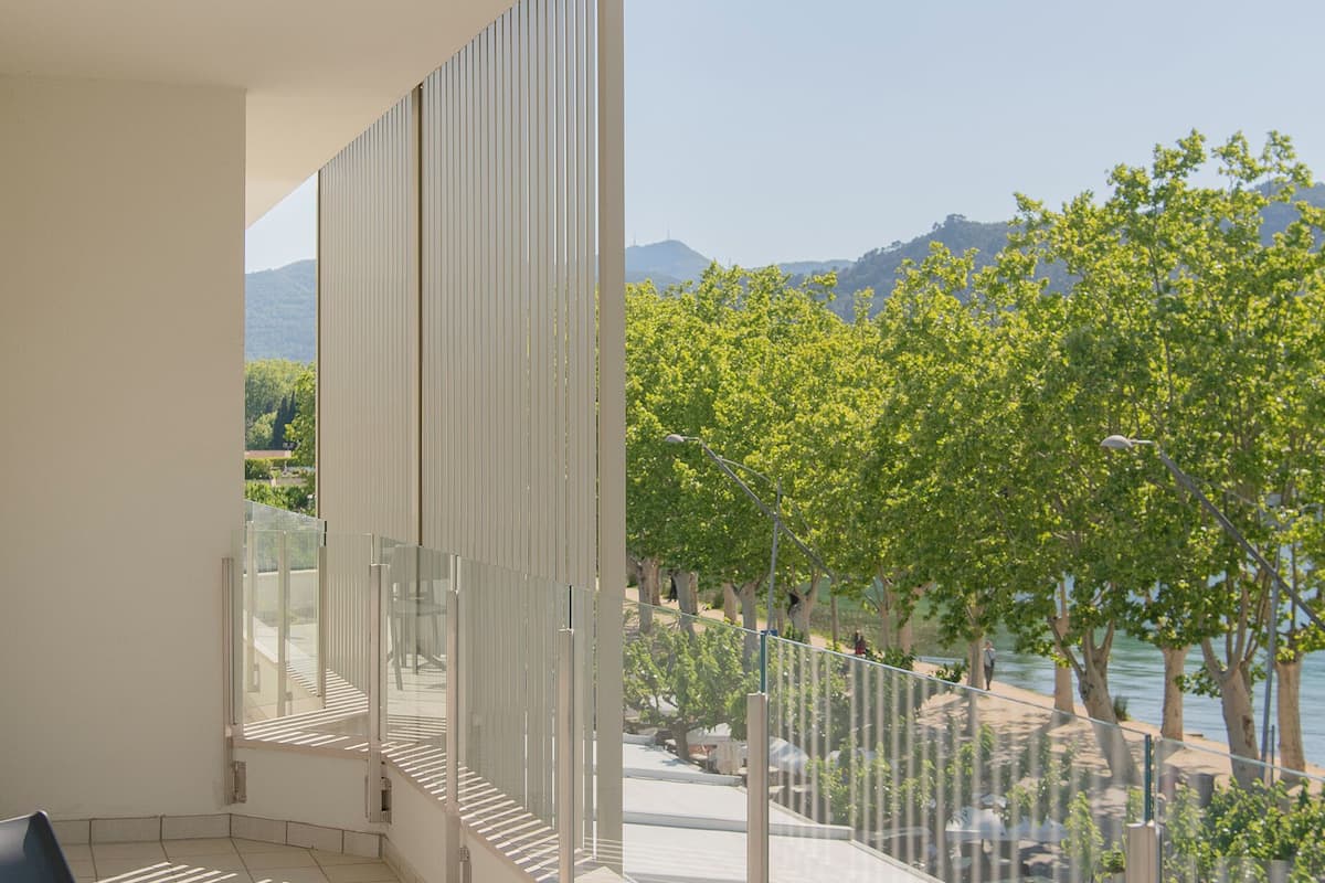 Un balcon avec une table et des chaises, une vue sur les arbres et les montagnes, et une balustrade.