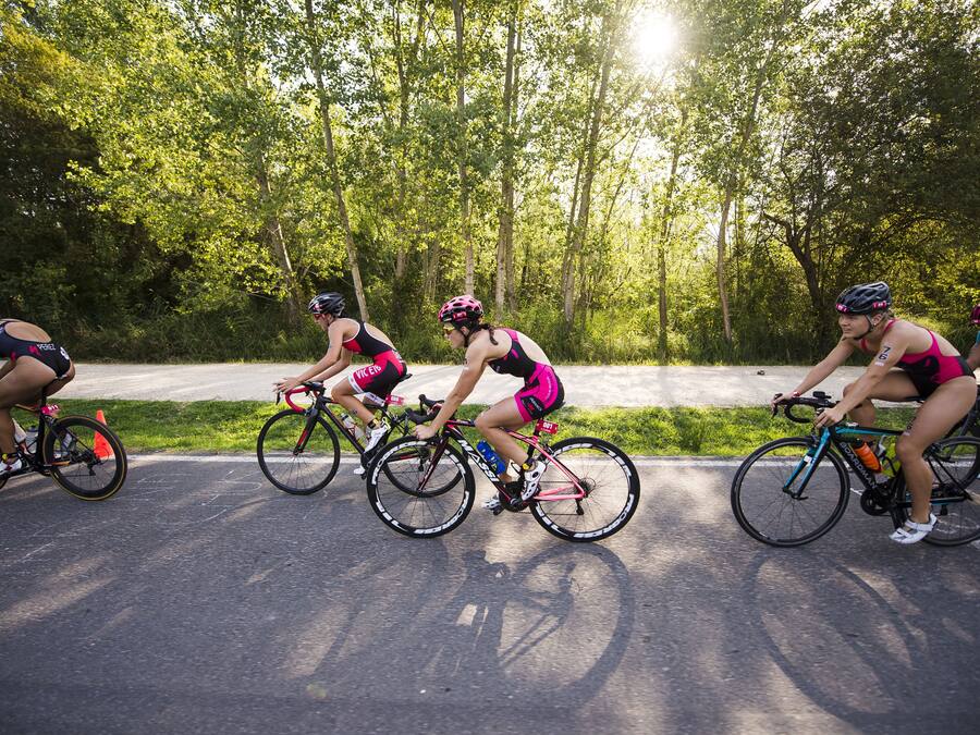 A group of cyclists riding on a paved path surrounded by trees.