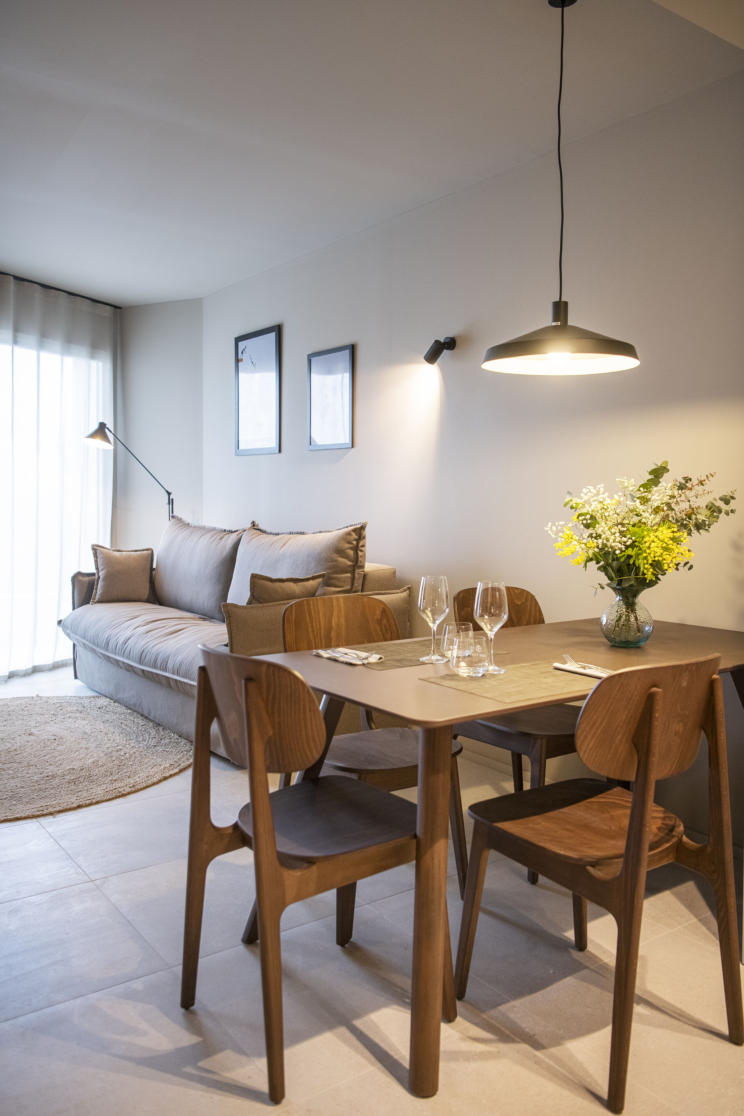 Una sala de estar moderna con una mesa de comedor, sillas, un sofá y un jarrón con flores.