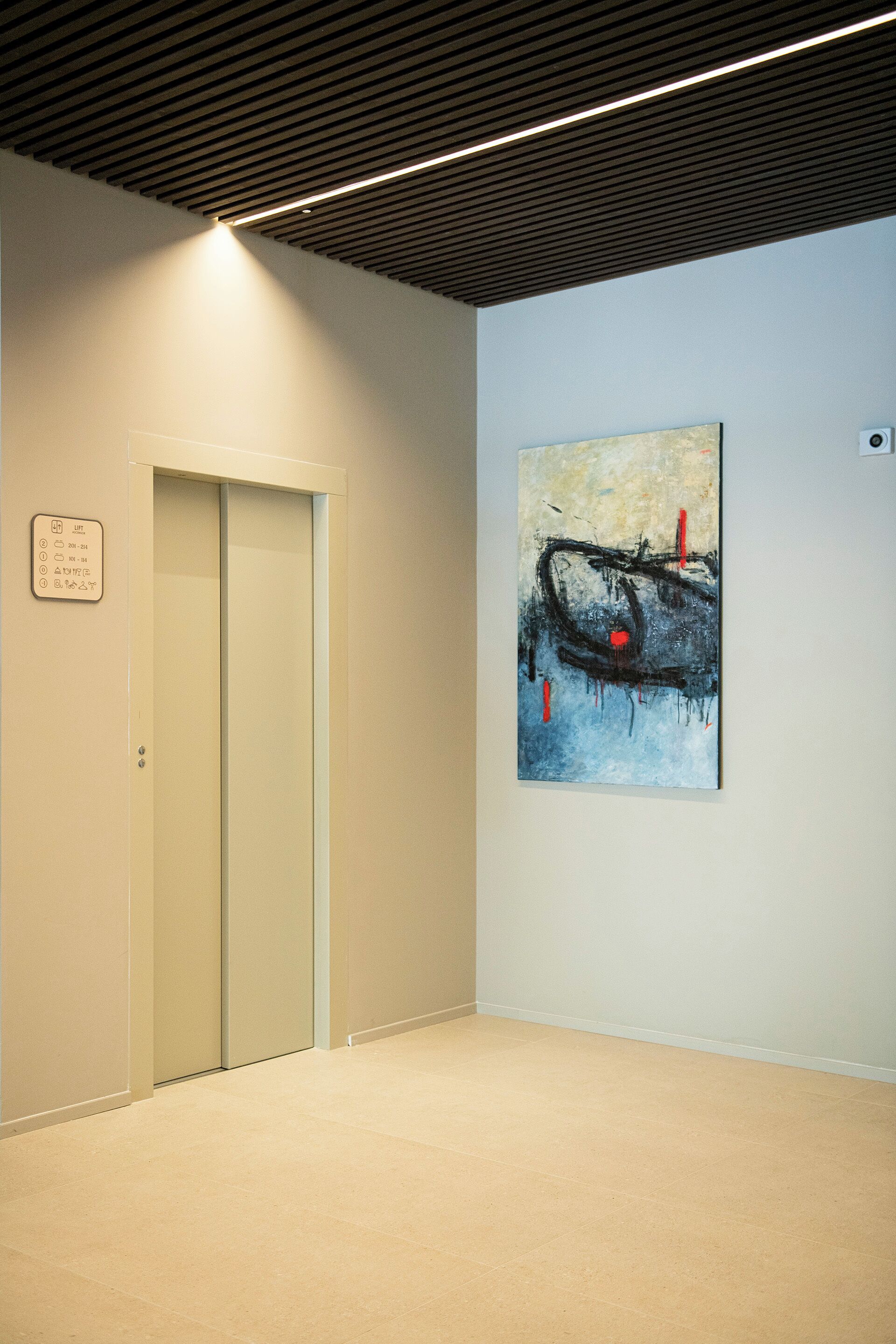 A hallway with a beige carpet, a closed door, and a wall-mounted artwork.