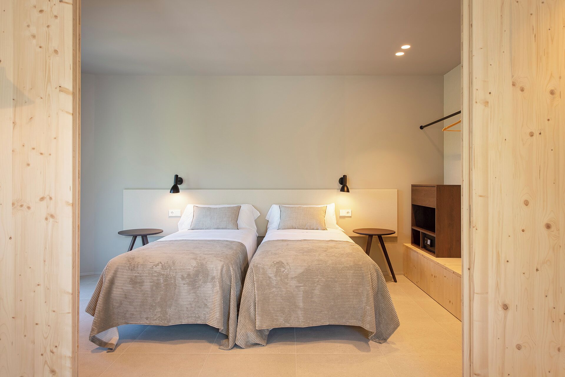 Une chambre moderne avec deux lits, chacun doté d’une tête de lit, de tables de chevet et de lampes fixées au mur.