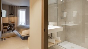 Een moderne hotelkamer met een bed, een bureau, een stoel, een televisie en een badkamer met een douchecabine van glas.