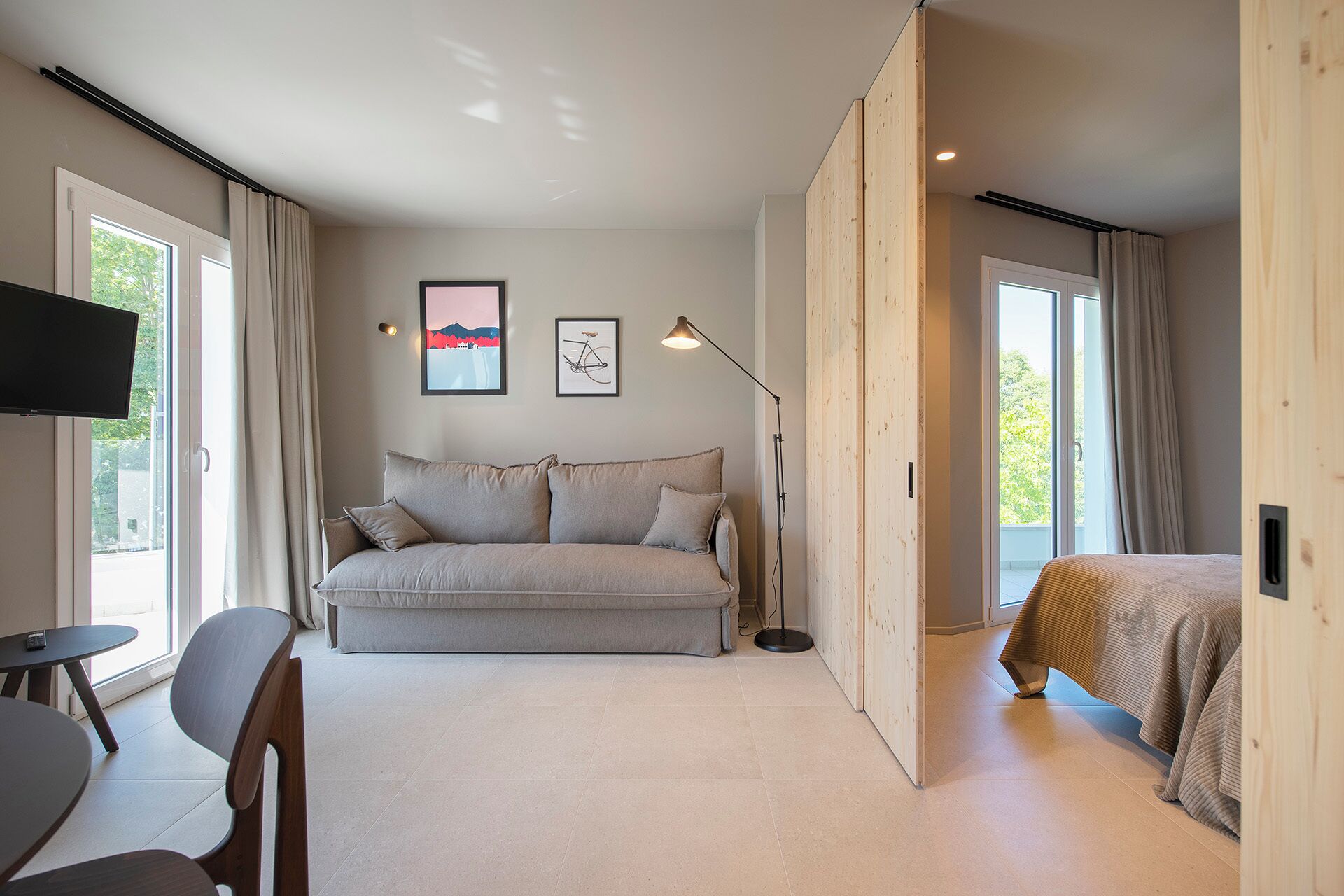 A modern bedroom with a sofa, a bed, a TV, and artwork on the wall.