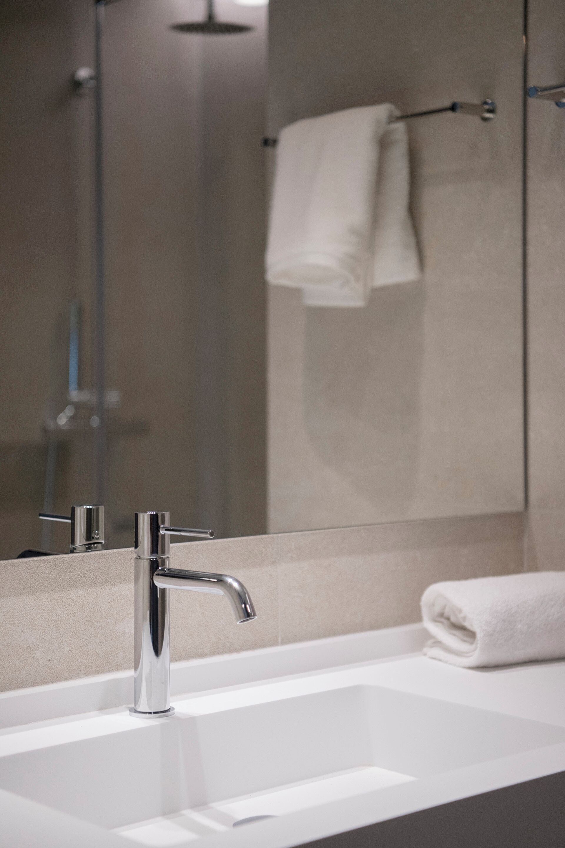 A modern bathroom with a white sink, chrome faucet, and a towel rack.