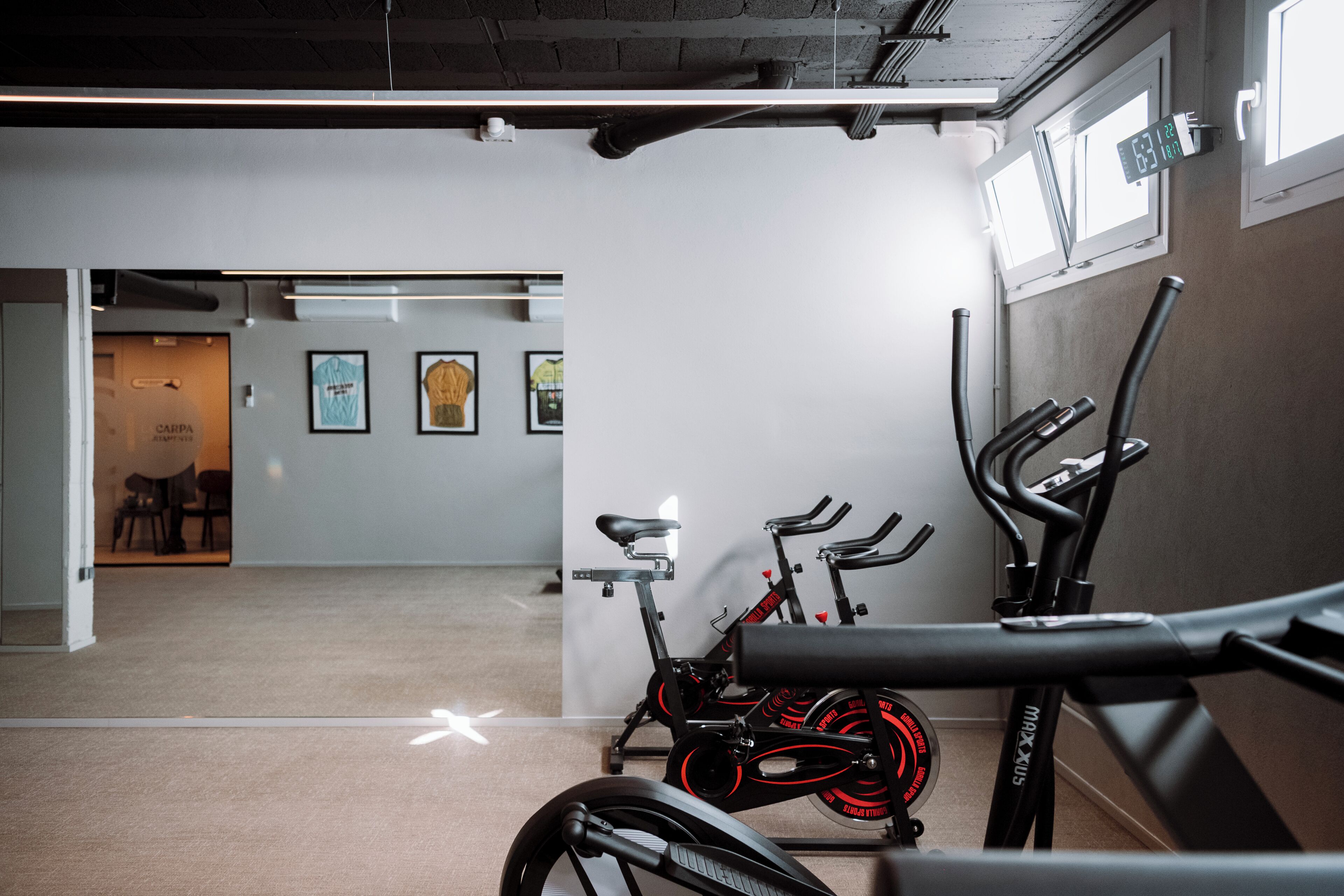 A gym with stationary bikes, a treadmill, and a wall-mounted digital clock.
