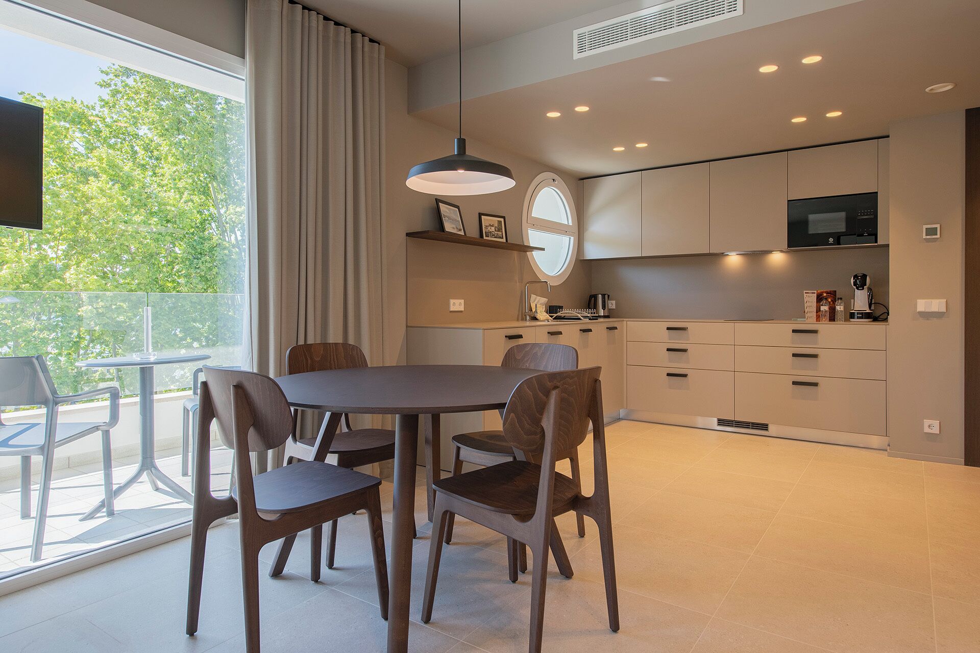 Una cocina moderna con comedor, con una mesa redonda y sillas, un gran ventanal con cortinas y electrodomésticos integrados.