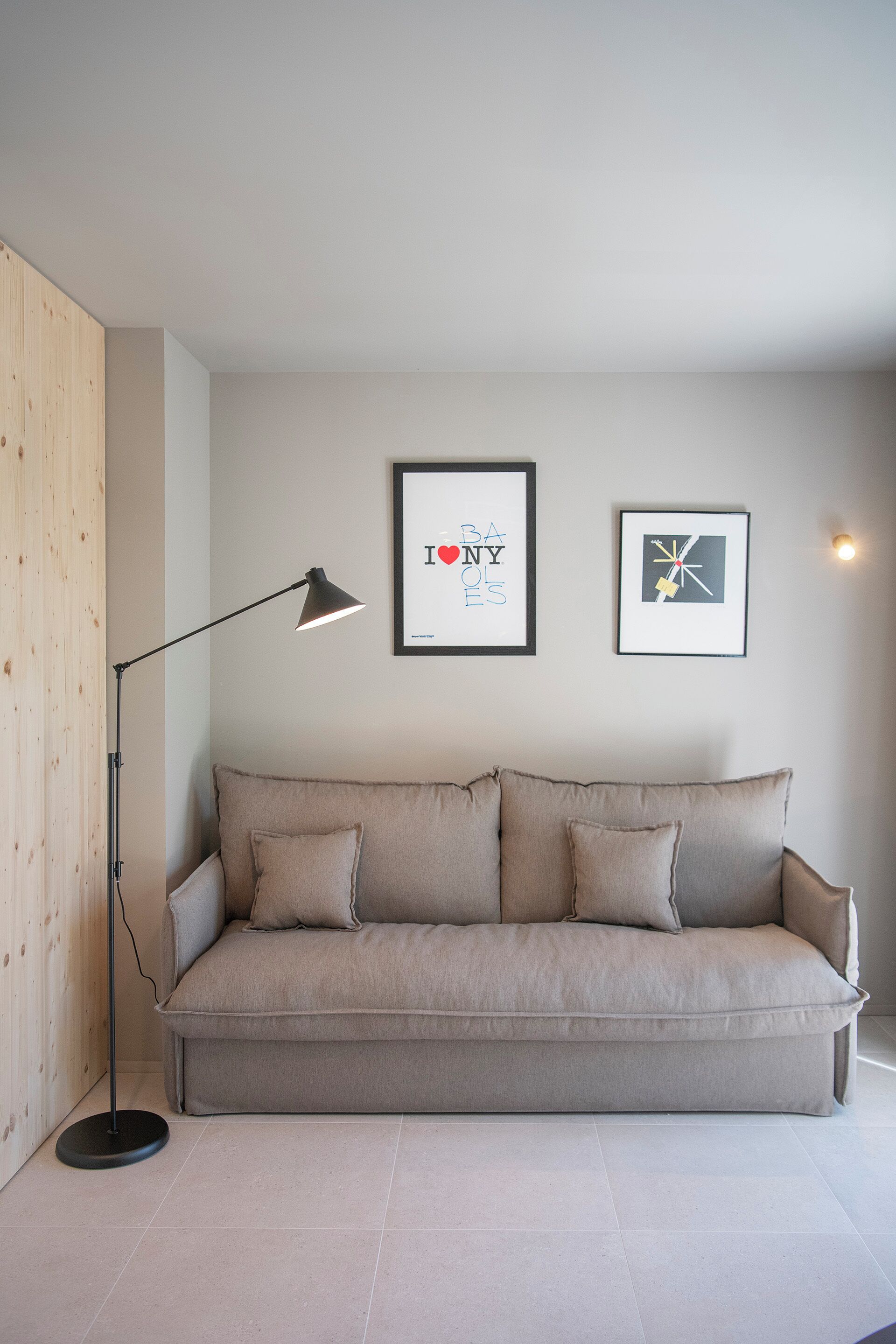 A neutral-toned living room with a sofa, a floor lamp, and two framed artworks on the wall.
