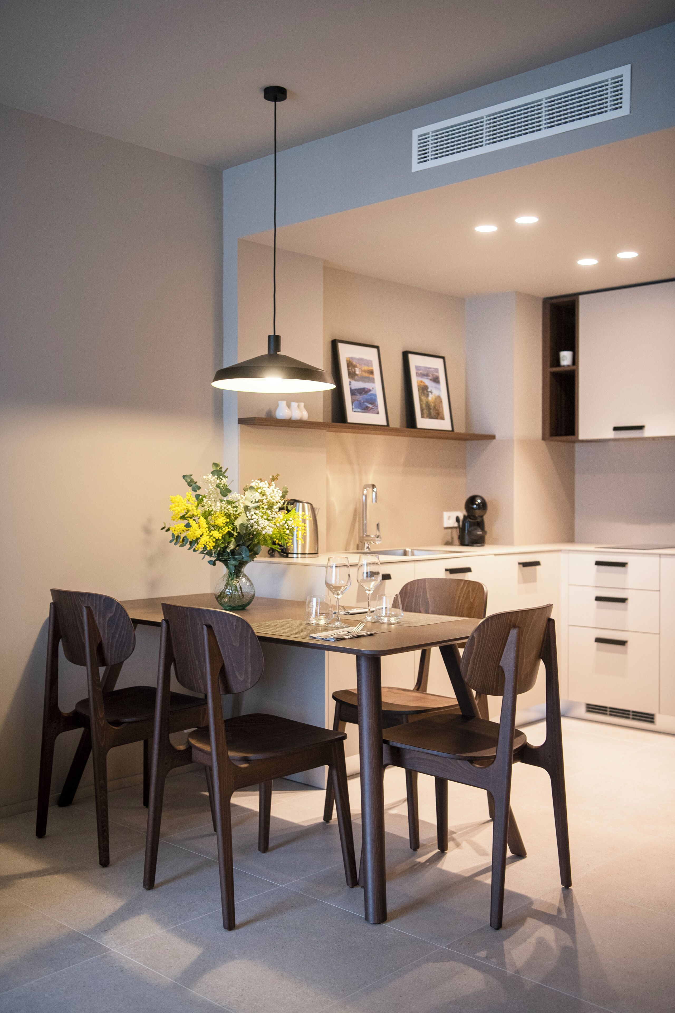 Una cucina moderna con mobili bianchi, un tavolo da pranzo con quattro sedie e una lampada a sospensione sopra.