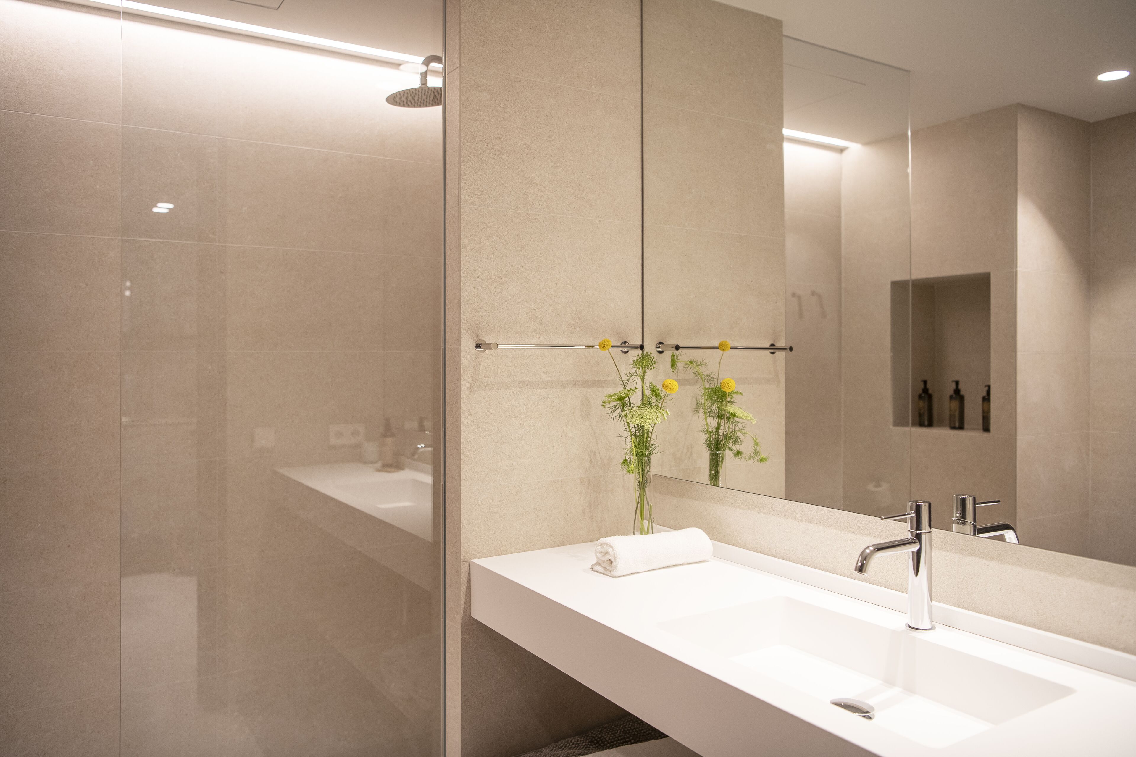 Un baño moderno con un espejo grande, un lavamanos blanco y un box de ducha de vidrio.