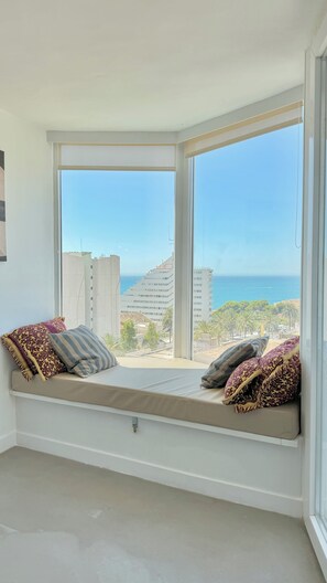 A room with a built-in bench seat overlooking a beach and buildings.