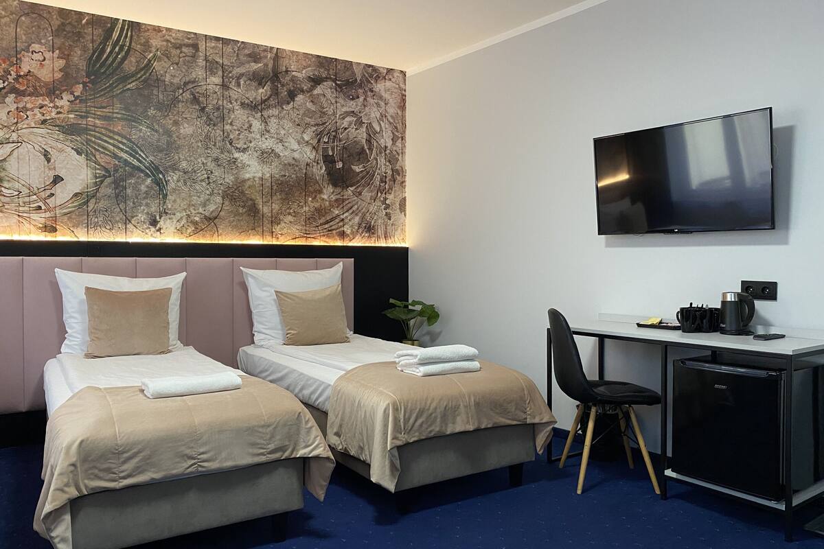 A hotel room with two beds, a desk, a chair, a television, and a large abstract painting on the wall.