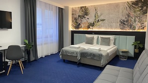 A hotel room with a bed, a desk, a chair, a sofa, and a large wall mural. - Cube House Aparthotel (Kraków)