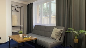 A modern living room with a grey sofa, a wooden coffee table, a hanging wardrobe, and a window with curtains. - Cube House Aparthotel (Kraków)
