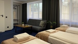 A hotel room with two beds, a sofa, a small table with a plant, and a wardrobe. - Cube House Aparthotel (Kraków)