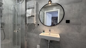 A modern bathroom with a glass shower enclosure, a white towel rack, a round mirror, and a white sink with a faucet. - Cube House Aparthotel (Kraków)