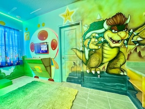 Una habitación con un mural de dinosaurios, una consola Nintendo Switch y un ventanal con cortinas.