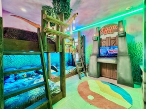 Una habitación con literas, una pared de escalada y una pantalla de televisión mostrando un juego.