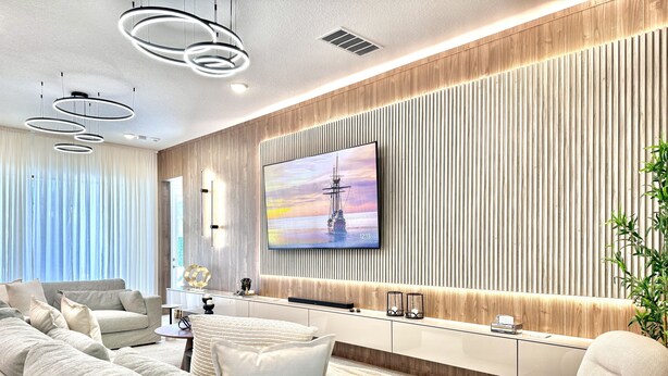 Un salon moderne doté d’un grand téléviseur à écran plat, d’un ensemble de canapés et d’un mur décoratif en bois.